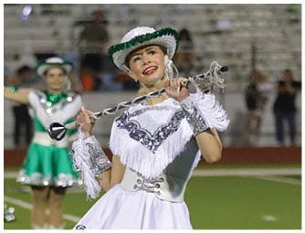 A person wearing a white and silver decorative uniform with boots is standing on a green sports field with white lines. Descripci n generada con IA