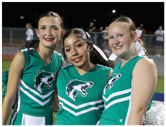 Two people wearing green cheerleading uniforms with a wolf logo and white stripes are smiling. Descripci n generada con IA