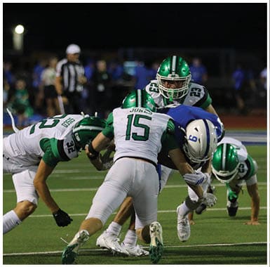Several people in football uniforms are engaged in a tackle during a nighttime game on a field. Descripci n generada con IA