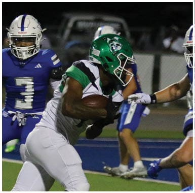 A person in a green and white football uniform is holding a football and running while another person in a blue and white uniform with the number three is behind them on a football field at night. Descripci n generada con IA