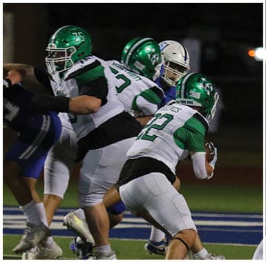 Three people wearing green and white football uniforms are engaged in a play on a football field at night. Descripci n generada con IA