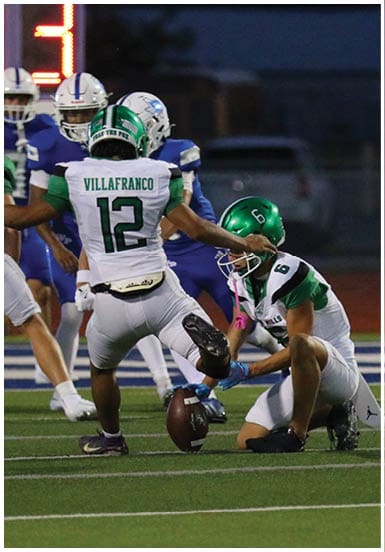 Two people in football uniforms with helmets are engaged in a play on a field, with one person reaching toward the other. Descripci n generada con IA