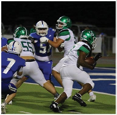 People wearing football uniforms are engaged in a game with one person holding the ball and others preparing to block or tackle. Descripci n generada con IA