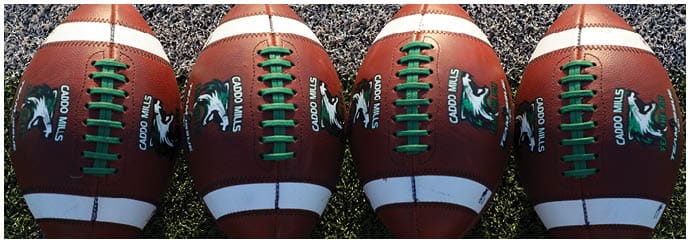 Four brown footballs with green laces are lined up closely on a textured surface. Descripci n generada con IA