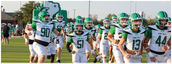 People in white and green football uniforms are running on a field, appearing to be warming up or entering a game. Descripci n generada con IA