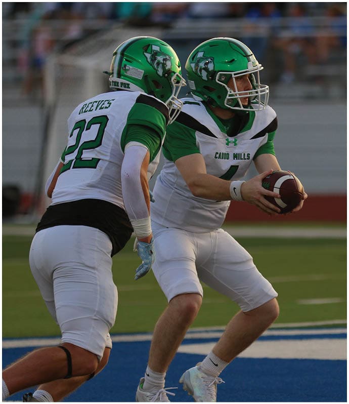 Two football players in green and white uniforms with helmets are on a field, with one player holding a football and preparing to make a play. Descripci n generada con IA