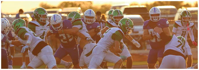 People wearing helmets and sports uniforms are actively engaged in a football game on a field during sunset. Descripci n generada con IA
