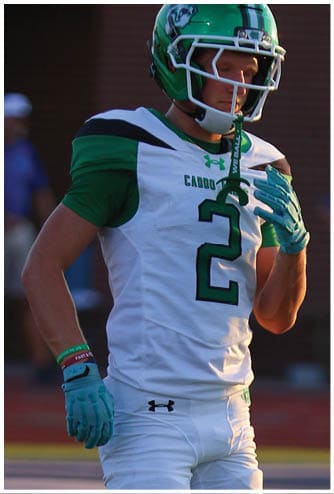 A person wearing a green football helmet and white sports jersey with green accents is looking downward. Descripci n generada con IA