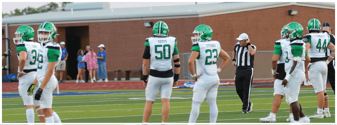 Several people in green and white football uniforms stand on a field near a referee wearing a black and white striped shirt and white cap. Descripci n generada con IA