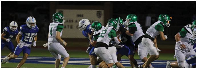 People wearing green and white uniforms are playing football against opponents in blue uniforms on a field at night. Descripci n generada con IA