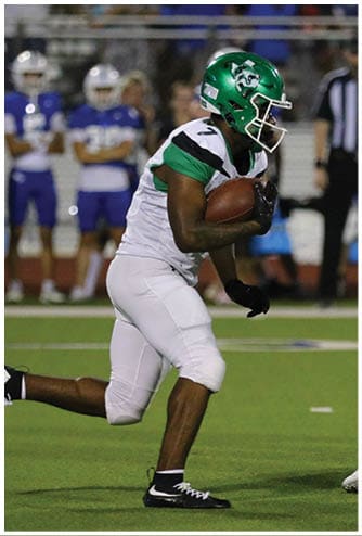 A person wearing a green helmet and white football uniform is holding a football and running on a field while another person in similar attire is nearby. Descripci n generada con IA
