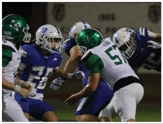 Three football players in green and white uniforms are engaged in a play against a player in a white helmet and blue uniform during a nighttime game. Descripci n generada con IA
