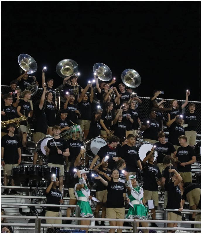 A group of people wearing matching black shirts and khaki pants are playing musical instruments and holding up phones with lights on in a stadium bleacher setting at night. Descripci n generada con IA