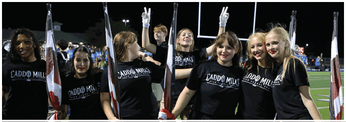 A group of people wearing matching black shirts with “Laddo Mills" text are standing on a sports field at night, some holding flags and making peace signs. Descripci n generada con IA