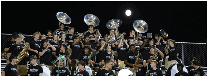 A large group of people wearing matching black shirts are playing various brass and percussion instruments in a band setting outdoors. Descripci n generada con IA