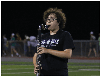 People wearing black shirts and khaki shorts are standing on a sports field holding musical instruments. Descripci n generada con IA