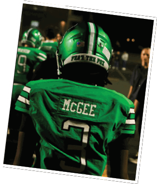 A person wearing a green football jersey with the name McGee and the number 3 on the back stands on a field with other people in the background. Descripci n generada con IA