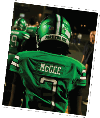 A person wearing a green football jersey with the name McGee and the number 3 on the back stands on a field with other people in the background. Descripci n generada con IA