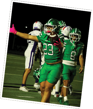 A person in a green football uniform with the number 23 is catching a football while extending one arm, with other players in green and white uniforms visible in the background on a football field at night. Descripci n generada con IA