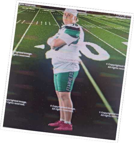 A person wearing a sports uniform and pink shoes stands with arms crossed on a football field under stadium lights. Descripci n generada con IA
