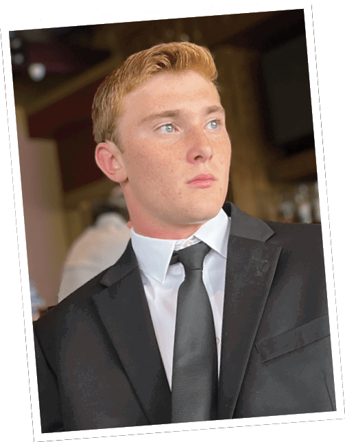 An adult with short hair wearing a black suit, white shirt, and black tie is looking to the side in an indoor setting. Descripci n generada con IA