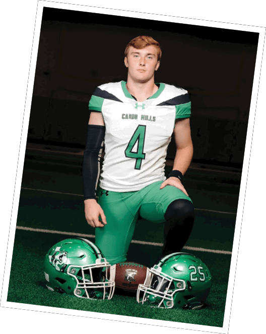 A person wearing a white and green football uniform with the number 4 kneels on a turf field between two green football helmets and a football. Descripci n generada con IA