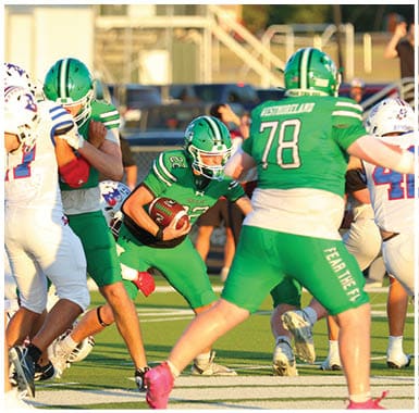 A person wearing a green football uniform with the number 22 is holding a football tightly while another player in a white helmet and uniform attempts to tackle them during a game. Descripci n generada con IA