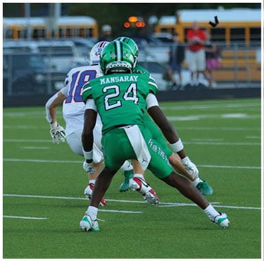 Two people in football uniforms are engaged in a play on a green field, with one wearing a green jersey labeled “MANSARAY 24" and the other in a white jersey numbered 18. Descripci n generada con IA