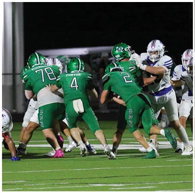 Several people wearing green and white football uniforms are engaged in a play on a well-lit football field at night. Descripci n generada con IA
