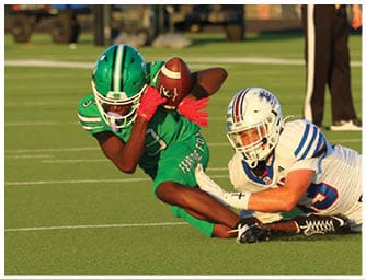 Two football players in green and white uniforms are on the ground during a game while a referee stands in the background on the field. Descripci n generada con IA