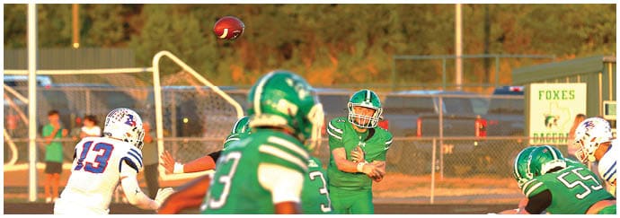 A group of people in football uniforms are playing on a field with one person throwing a football in mid-air during a game. Descripci n generada con IA