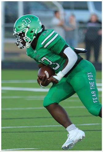 A person wearing a green football uniform and helmet is running on a field while holding a football. Descripci n generada con IA