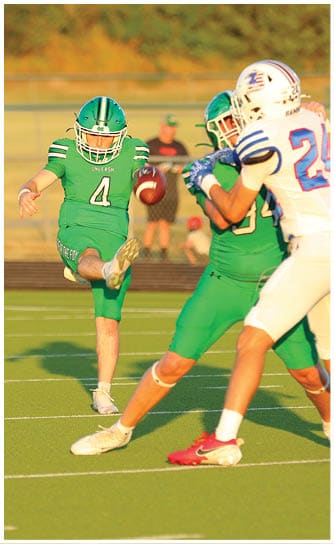 A person in green football gear is kicking a football on a field while another person in similar gear is nearby. Descripci n generada con IA