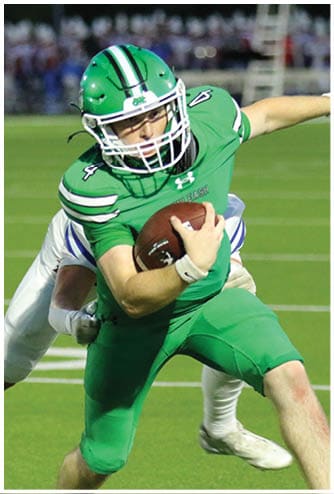 A person in green football gear is running with the ball while another person in white attempts to tackle them from behind on a grassy field. Descripci n generada con IA