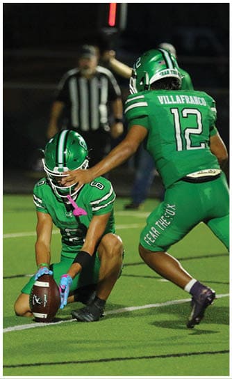 A person wearing a green football uniform and helmet is being touched on the head by another person's hand during a game. Descripci n generada con IA