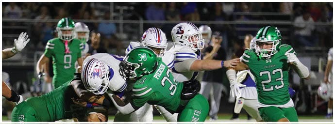 Players in green and white football uniforms are actively engaged in a play on a football field with a crowd in the background. Descripci n generada con IA