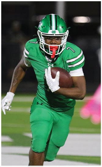 A person wearing a green football uniform is running while holding a football tightly against their body on a field. Descripci n generada con IA