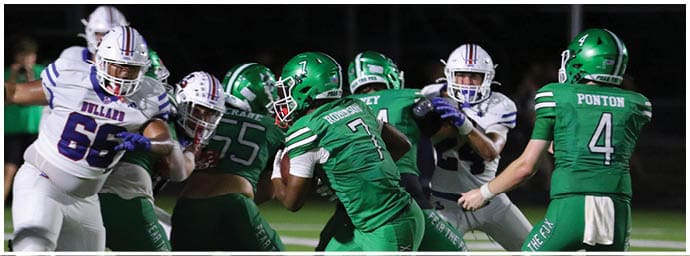 Players in green and white football uniforms are engaged in a play on a football field at night. Descripci n generada con IA