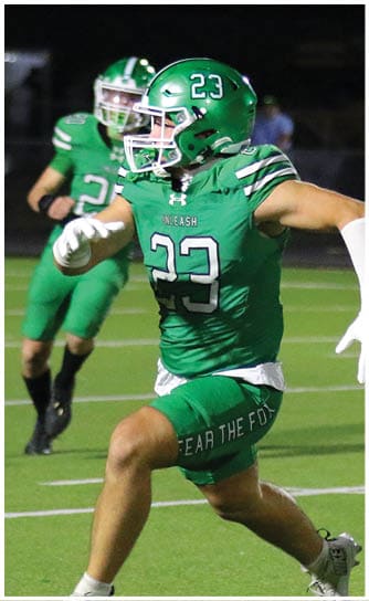 A person in a white football uniform with the number 16 is running on a field while another person in a green uniform is partially visible behind them. Descripci n generada con IA