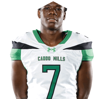Person wearing a white and green sports jersey with the number seven and the words “Caddo Mills" standing against a white background. Descripci n generada con IA