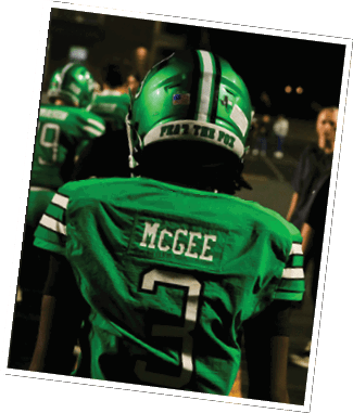 A person wearing a green football jersey with the name McGee and the number 3 on the back stands on a field with other people in the background. Descripci n generada con IA