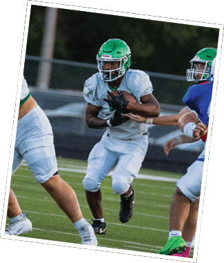 People wearing green and blue football uniforms are playing on a field with one person in green running with the ball while others block or pursue. Descripci n generada con IA