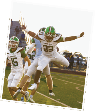 Two people in football uniforms celebrating on a field with one person jumping in the air and another person reaching out. Descripci n generada con IA