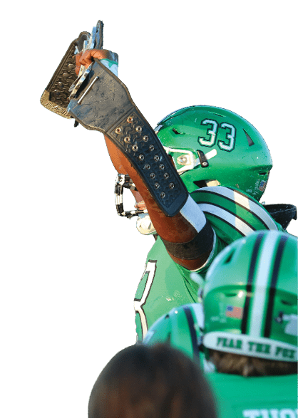 A person in a green football uniform with the number 33 raises one arm while two other players in green uniforms with the names Thorn and Bennett stand nearby on a field. Descripci n generada con IA