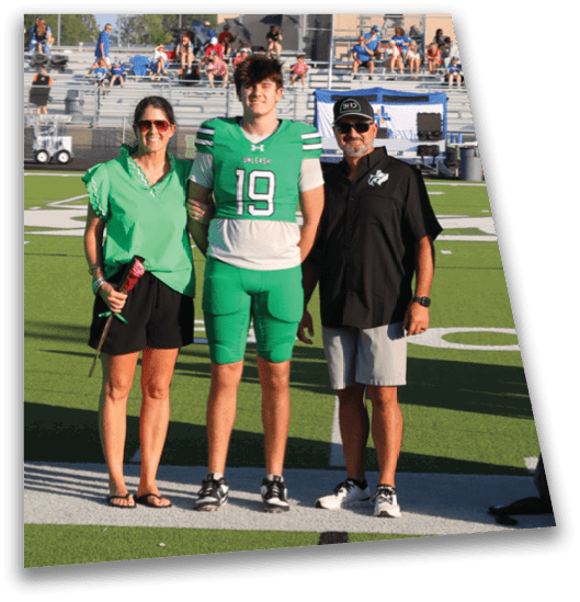 Three people stand on a sports field under a large green inflatable arch shaped like the state of Texas with a wolf logo and the word “FOXES" on the sides. Descripci n generada con IA