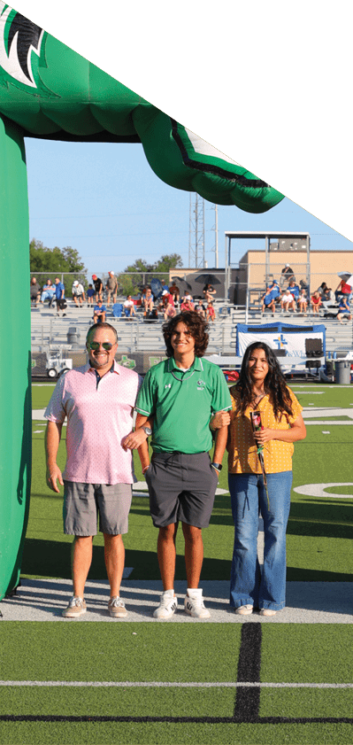 Tres personas est n de pie sonrientes bajo una estructura inflable verde y blanca con la forma del estado de Texas y un logo de un lobo rugiendo en un campo deportivo. Descripci n generada con IA