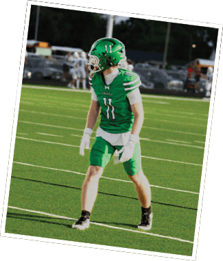 Two people in green and white football uniforms with helmets are on a field, one flexing their arms while the other stands nearby. Descripci n generada con IA