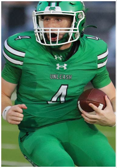 A person wearing a green football uniform with the number 4 is running on a football field while holding a football. Descripci n generada con IA