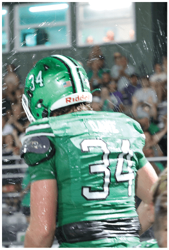A person wearing a green sports jersey with the number 34 is in the foreground while a crowd of people watches in the background. Descripci n generada con IA