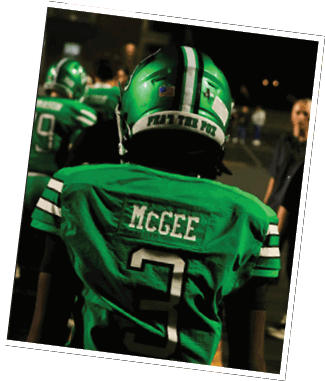 A person wearing a green football jersey with the name McGee and the number 3 on the back stands on a field with other people in the background. Descripci n generada con IA